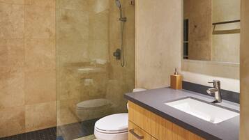 Un baño moderno con ducha envuelta en vidrio, inodoro blanco y muebles de madera.