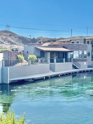 A waterfront property with a pool, a covered patio, and a view of the hills.