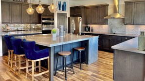 Une cuisine moderne avec des meubles de couleur bois foncé, un plan de travail en marbre et un grand îlot central doté de tabourets de bar.