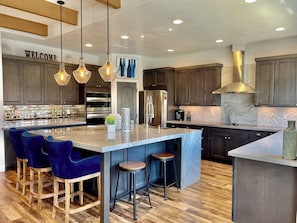 A modern kitchen with dark wood cabinets, a large island with bar stools, a stainless steel oven, and a 'WELCOME' sign.
