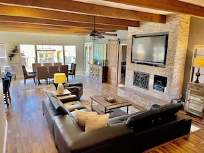 A spacious living room with a large black leather sofa, a coffee table, and a fireplace with a TV mounted above it.