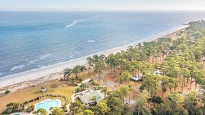 An aerial view of a coastal property with a swimming pool, beachfront, and dense forest.