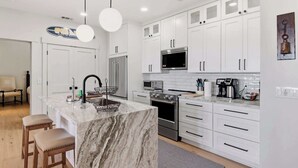 A modern kitchen with white cabinetry, a marble island, stainless steel appliances, and a dining area with wooden stools.