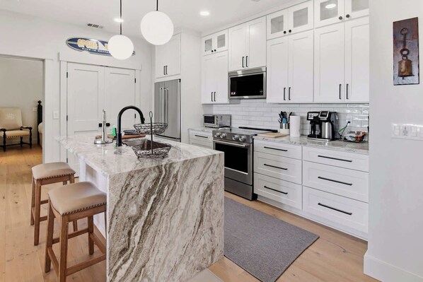 A modern kitchen with white cabinetry, a marble island, stainless steel appliances, and a dining area with wooden stools.