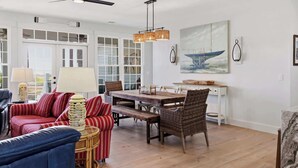 A spacious living room with a dining area, large windows, and a ceiling fan.