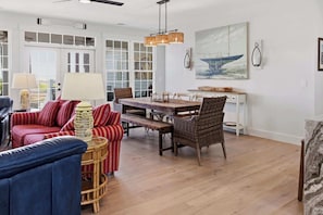 A spacious living room with a dining area, large windows, and a ceiling fan.