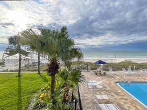 A poolside area with lounge chairs, a pool, and a view of the beach. - BEAUTIFUL CONDO WITH BALCONY FACING GULF OF MEXICO WITH BRAND NEW HEATED POOL (Indian Rocks Beach)