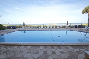 Une piscine avec une terrasse carrelée, des chaises longues et une vue sur la mer.
