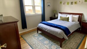 Une chambre à coucher comprenant un lit, une table de chevet, une lampe, une fenêtre avec des rideaux, une porte et un tapis.