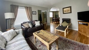 Un salon avec un canapé, une table basse, un téléviseur et, au fond, un coin repas.
