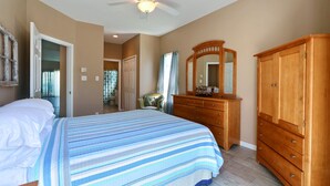 Une chambre à coucher avec un lit, une commode en bois, un miroir et un ventilateur de plafond.