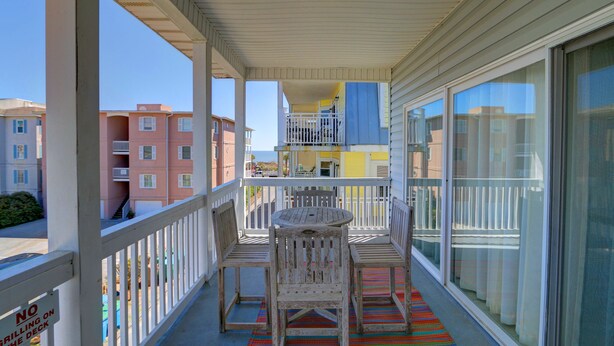 Un balcon avec des balustrades blanches, une table en bois et deux chaises.