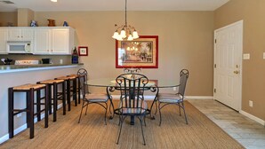 Un coin repas avec une table ronde et des chaises, une cuisine avec des meubles blancs et un luminaire suspendu.