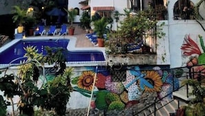 A hotel courtyard with a swimming pool, outdoor seating, and a mural.