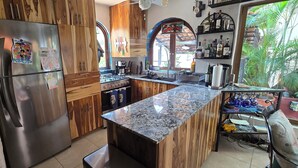 A kitchen with wooden cabinets, a stainless steel refrigerator, a granite countertop, and a coffee machine.