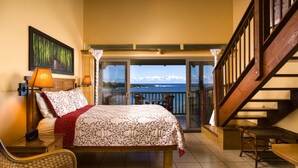 A bedroom with a bed, bedside lamps, a chair, and a view of the ocean through a glass door.