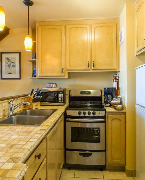 Una cocina con gabinetes de madera, un lavamanos de acero inoxidable, un microondas, una estufa y un refrigerador.
