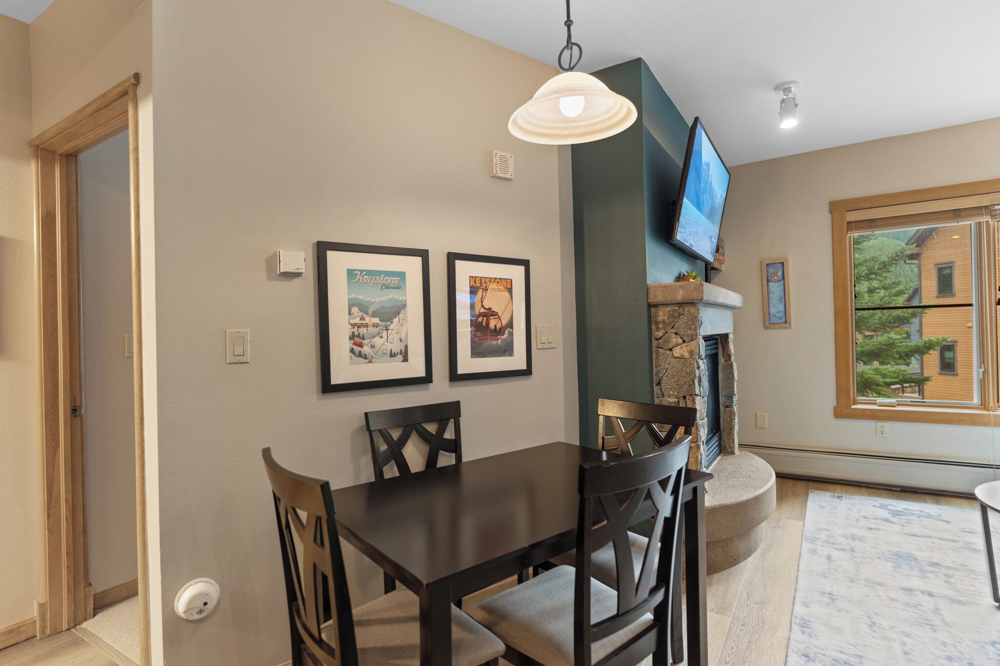 A dining area with a table and chairs, a mounted television, and framed pictures on the wall.