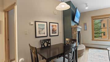 A dining area with a table and chairs, a mounted television, and framed pictures on the wall.