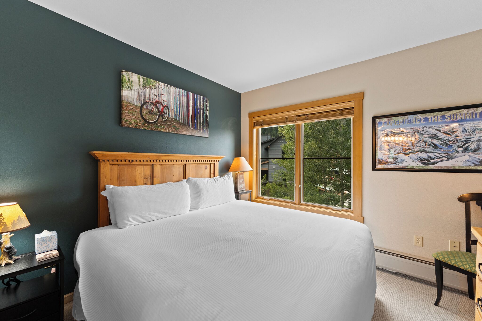 A bedroom with a large bed, a wooden headboard, a window with a view, and a painting on the wall.