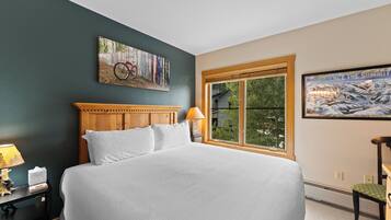 A bedroom with a large bed, a wooden headboard, a window with a view, and a painting on the wall.