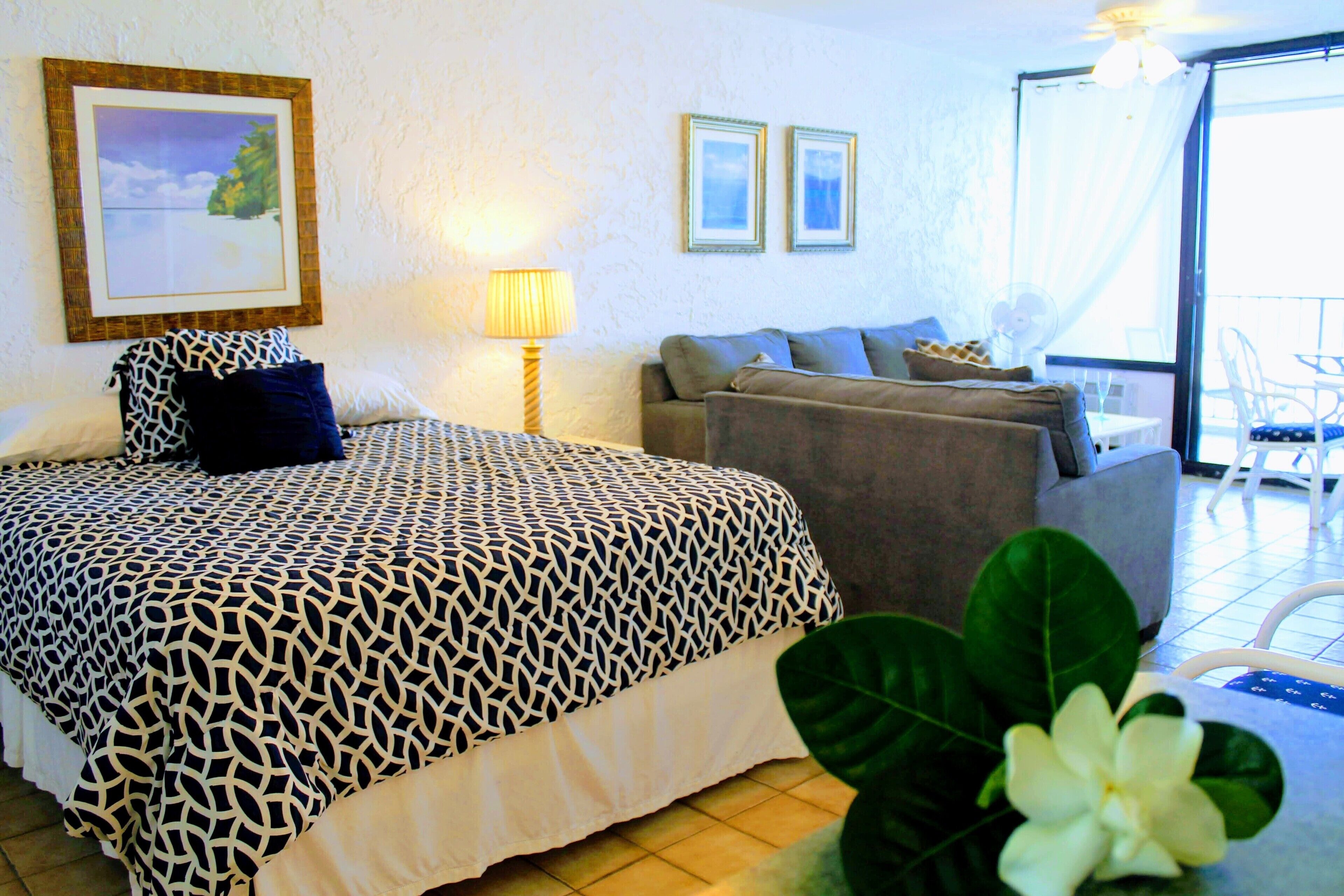 A hotel room with a bed, a sofa, a dining table, and a balcony with chairs.