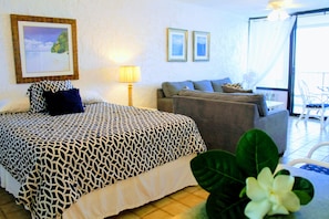 Quarto de hotel com cama, sofá, mesa de jantar e varanda com cadeiras.