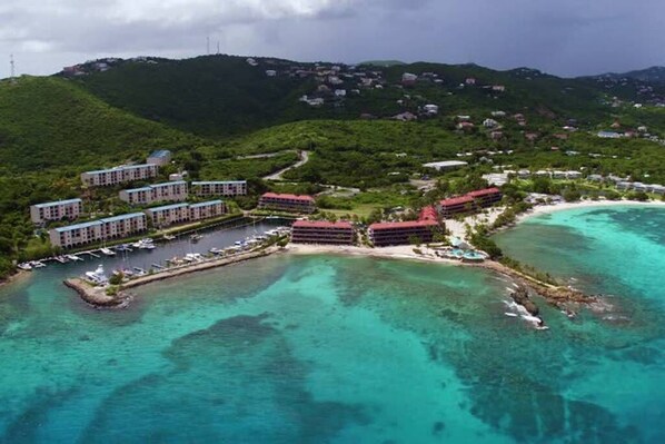 An aerial view of a coastal resort with multiple hotel buildings, a marina, and clear turquoise waters.
