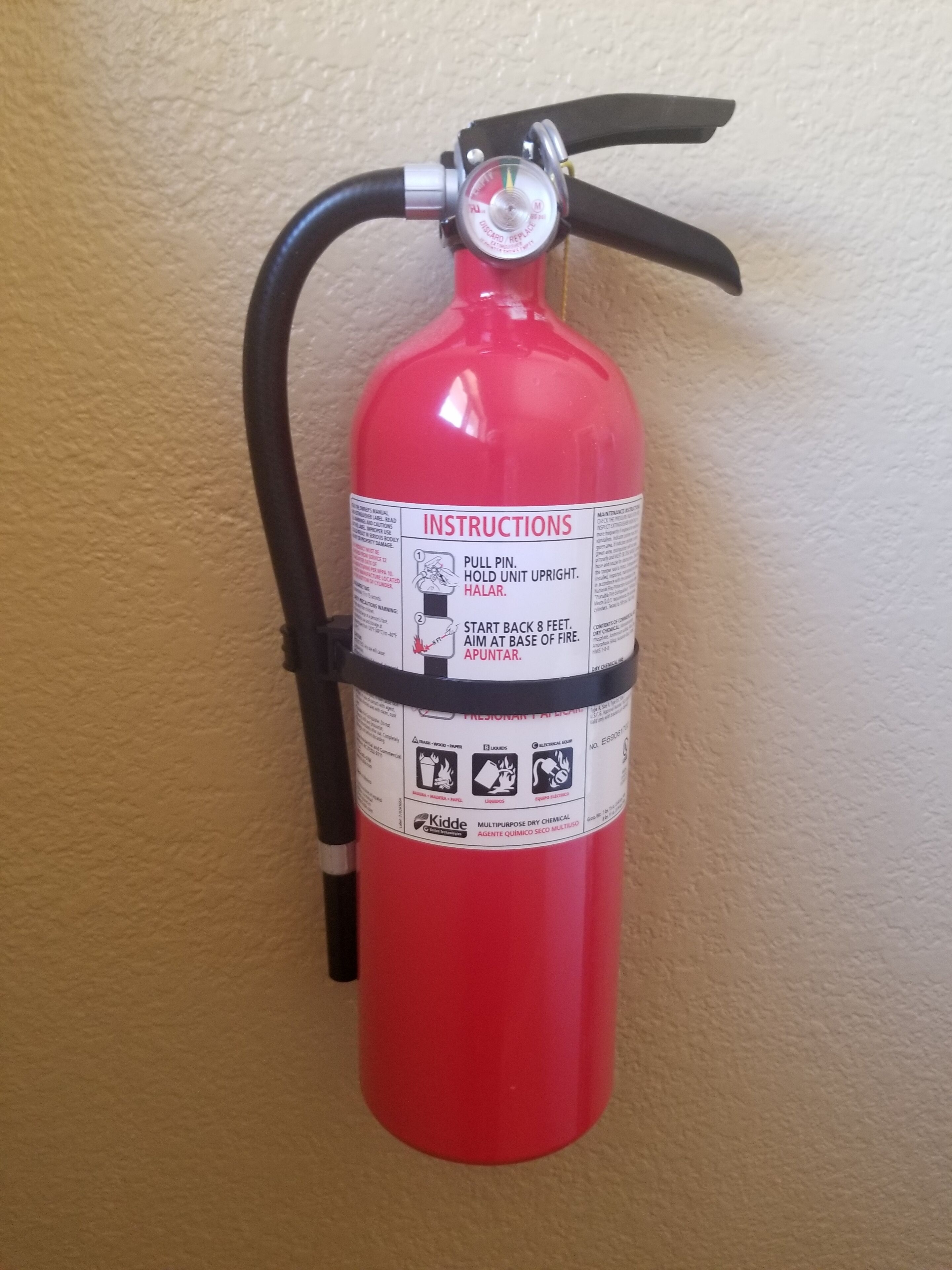 Um extintor de incêndio vermelho fixado na parede com instruções e símbolos de segurança.