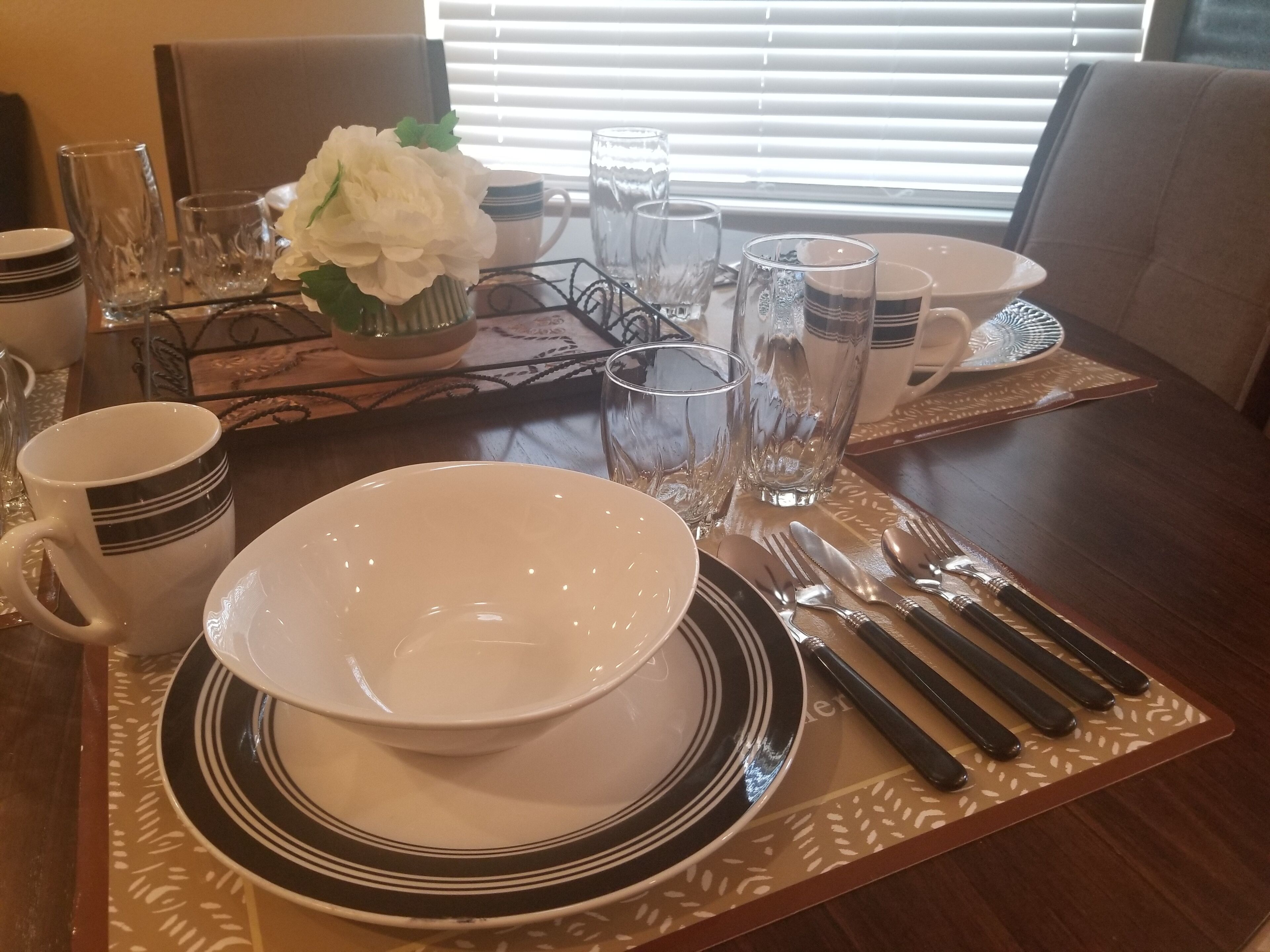 A dining table set with white plates, black and white striped cups, and clear glasses.