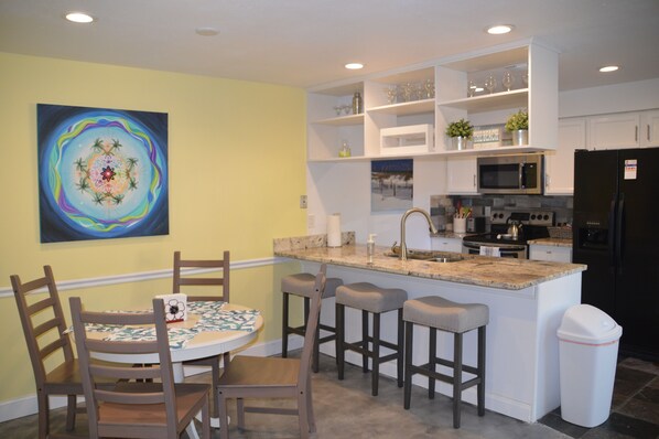 Una cocina con una isla central, taburetes de bar, un microondas y un refrigerador.