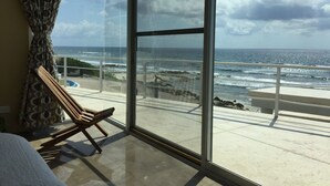 A balcony with a view of the ocean, a wooden chair, and a glass door. - Early Holiday Booking Discount! (Tulum)