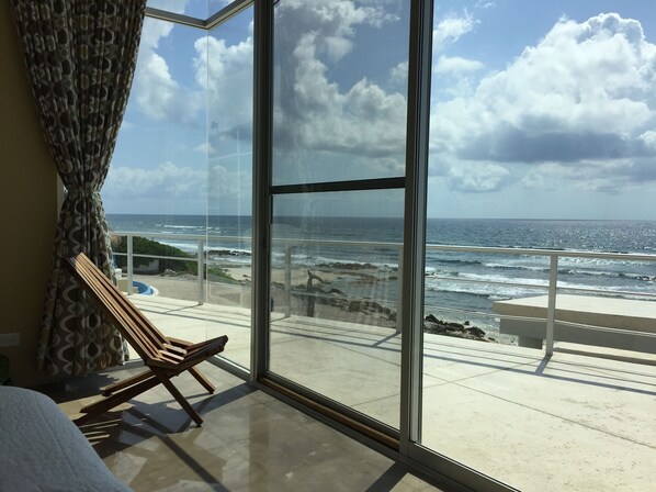 A balcony with a view of the ocean, a wooden chair, and a glass door. - Early Holiday Booking Discount! (Tulum)