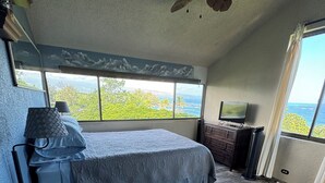 Een slaapkamer met een bed, een plafondventilator, een televisie en uitzicht op de oceaan.