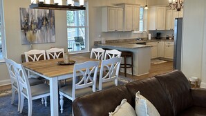 A modern kitchen with white cabinets, a dining area with a wooden table and white chairs, and a brown leather sofa with cushions. - Lakefront Southern Charm with private dock (Pinetta)