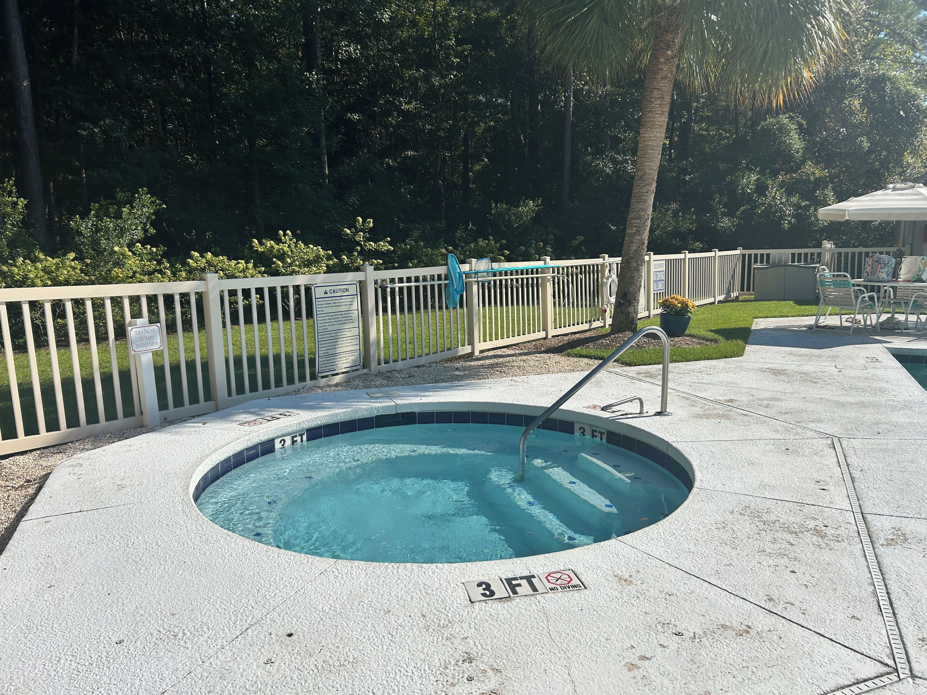 Una piscina pequeña y redonda con un indicador de profundidad de 3 pies, rodeada por una valla blanca y un cartel que dice 'No saltar al spa'.