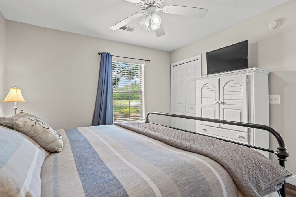 A bedroom with a bed, a ceiling fan, a wardrobe, and a window with curtains.