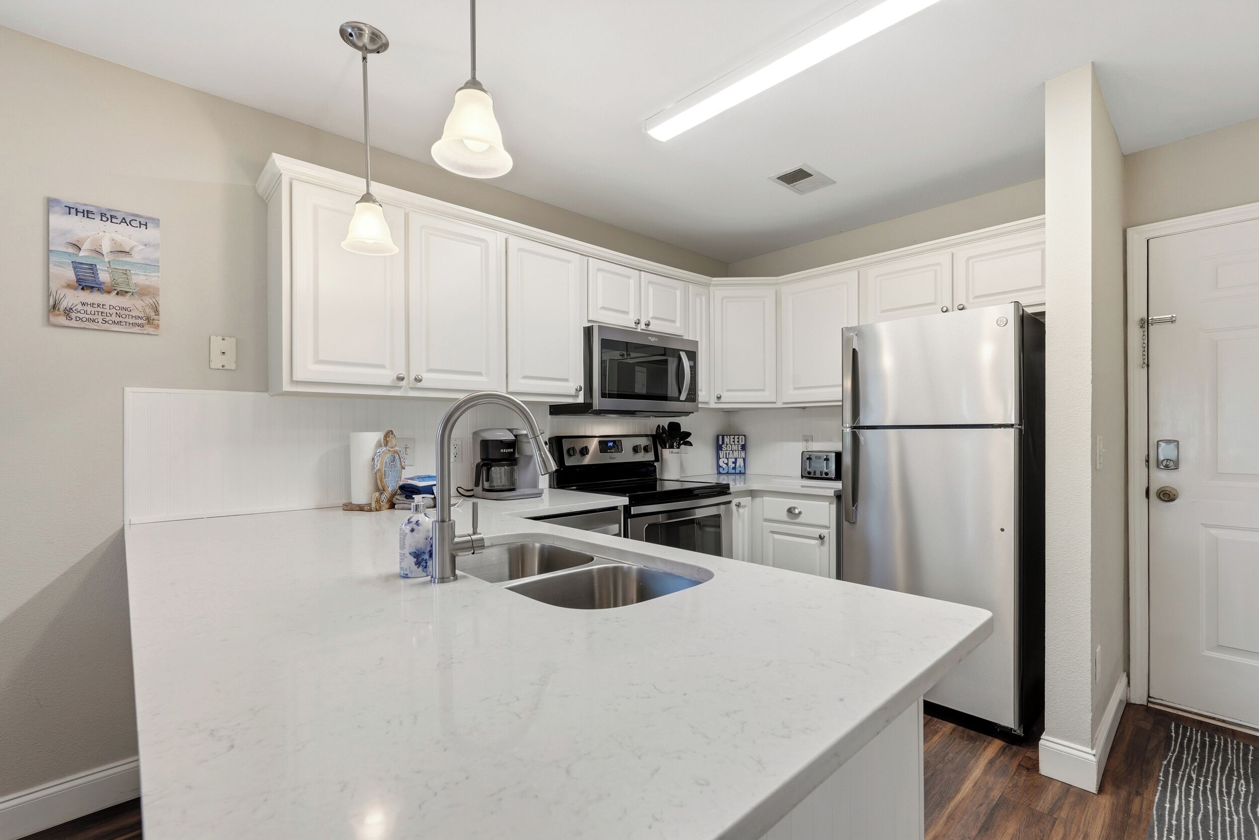 A modern kitchen with white cabinetry, stainless steel appliances, a double sink, and pendant lighting.