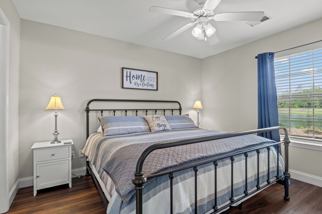 A bedroom with a bed, two bedside tables, a ceiling fan, and a window with curtains.