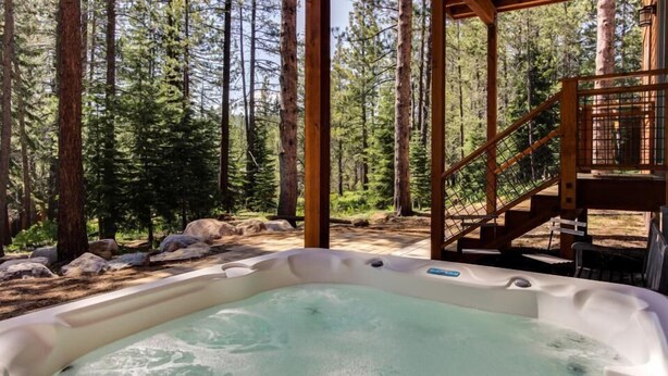 A hot tub in a forested area with a wooden deck and stairs leading up to it. - Tahoe Donner modern: Perfect for 3 families! 3 King/6 Twin. 4 BA, Cook's Kitchen (Truckee)