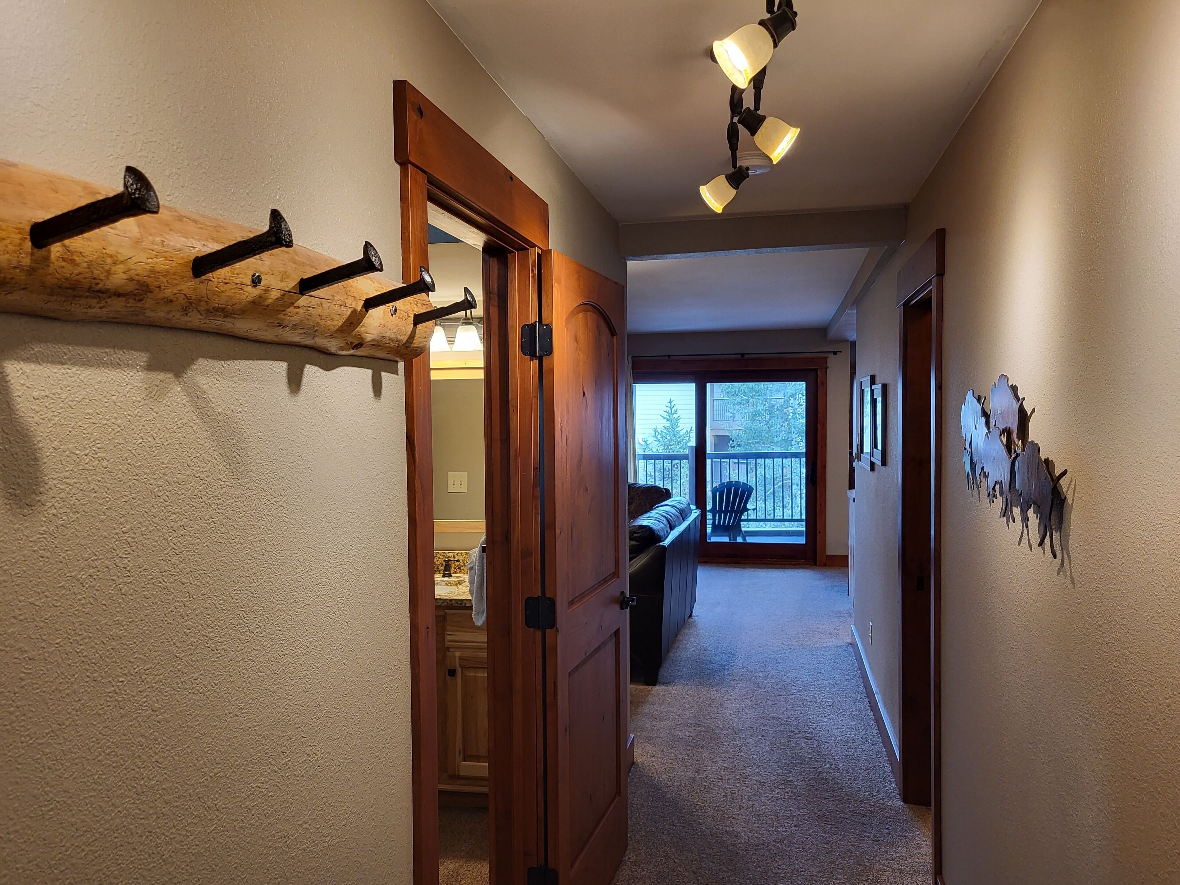 Un couloir avec un porte-manteau en bois, un banc et une porte donnant sur un balcon.