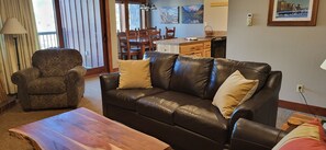 Una sala de estar con un sofá de cuero, una mesa de centro de madera y un sillón estampado.