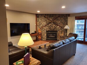 Una sala de estar con pared de piedra, chimenea, sofá de cuero y televisor de pantalla plana.