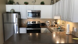 Una cocina con armarios blancos, electrodomésticos de acero inoxidable, encimera de granito y cafetera.