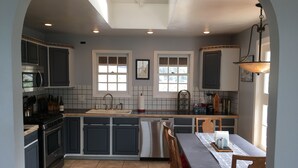 A modern kitchen with dark cabinets, a central island, and a dining area with a table and chairs. - Best views on Sonoma Coast!Oceanfront,private hot tub, fire pit, pets considered (Bodega Bay)