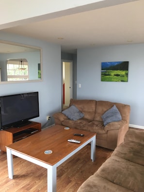 A living room with a brown sofa, a wooden coffee table, a flat-screen TV, and a painting on the wall. - Best views on Sonoma Coast!Oceanfront,private hot tub, fire pit, pets considered (Bodega Bay)