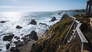 A coastal view with rocky terrain and a wooden walkway leading to a building with a large window overlooking the ocean. - Best views on Sonoma Coast!Oceanfront,private hot tub, fire pit, pets considered (Bodega Bay)