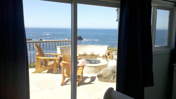 A balcony with a view of the ocean, featuring chairs, a fire pit, and a stone fireplace. - Best views on Sonoma Coast!Oceanfront,private hot tub, fire pit, pets considered (Bodega Bay)