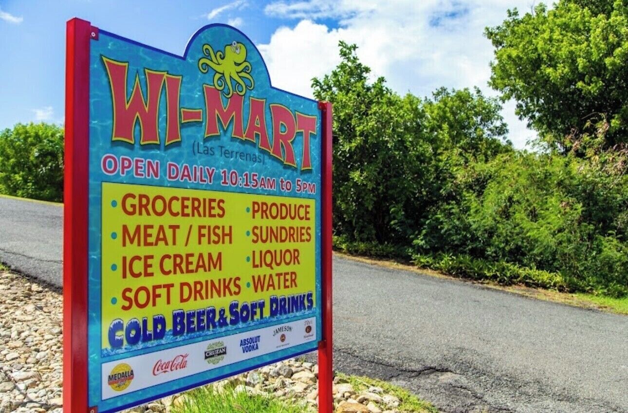 A WI-MART sign listing its operating hours and available products like groceries, meat, ice cream, and cold beers.