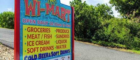 A WI-MART sign listing its operating hours and available products like groceries, meat, ice cream, and cold beers.